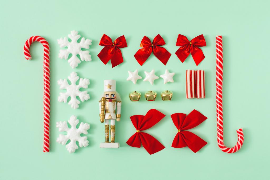 Una colección de artículos festivos sobre un fondo verde claro. Incluye bastones de caramelo, copos de nieve, lazos rojos, una figura de Cascanueces, campanillas doradas, estrellas blancas y un regalo a rayas.